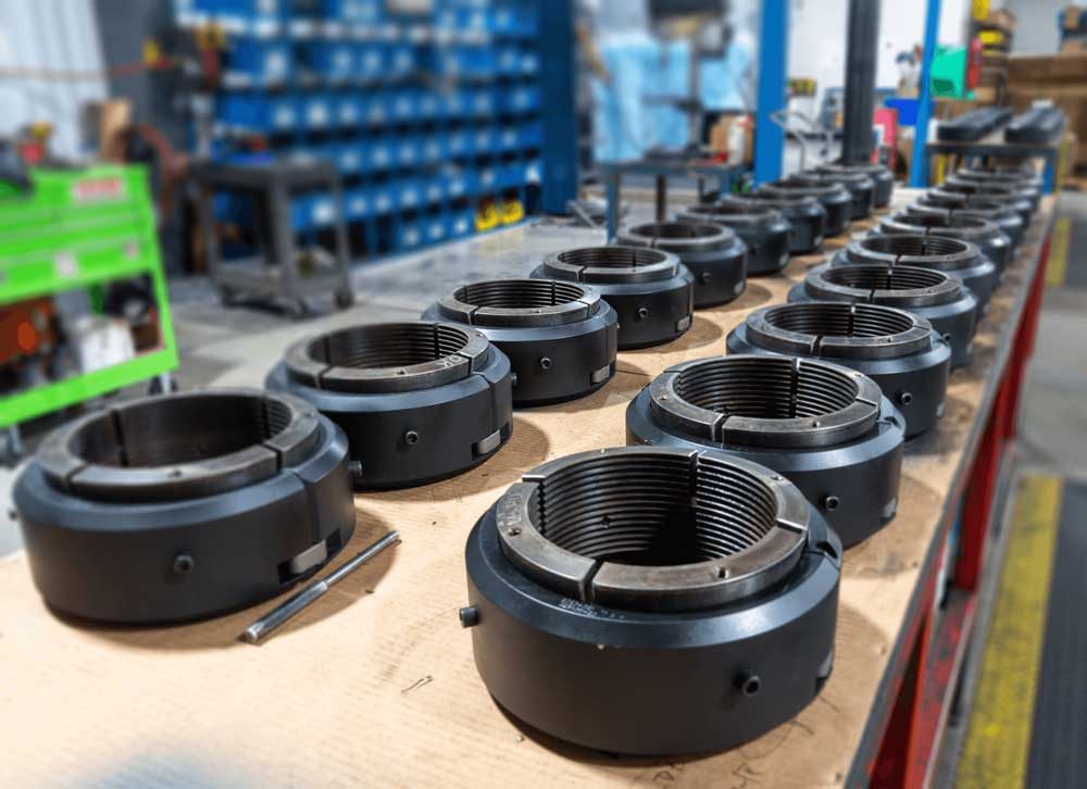 CAMTOP C-21 casing hanger production run — rows of black slip-type casing hangers with threaded slip bowls arranged on workshop bench in manufacturing facility